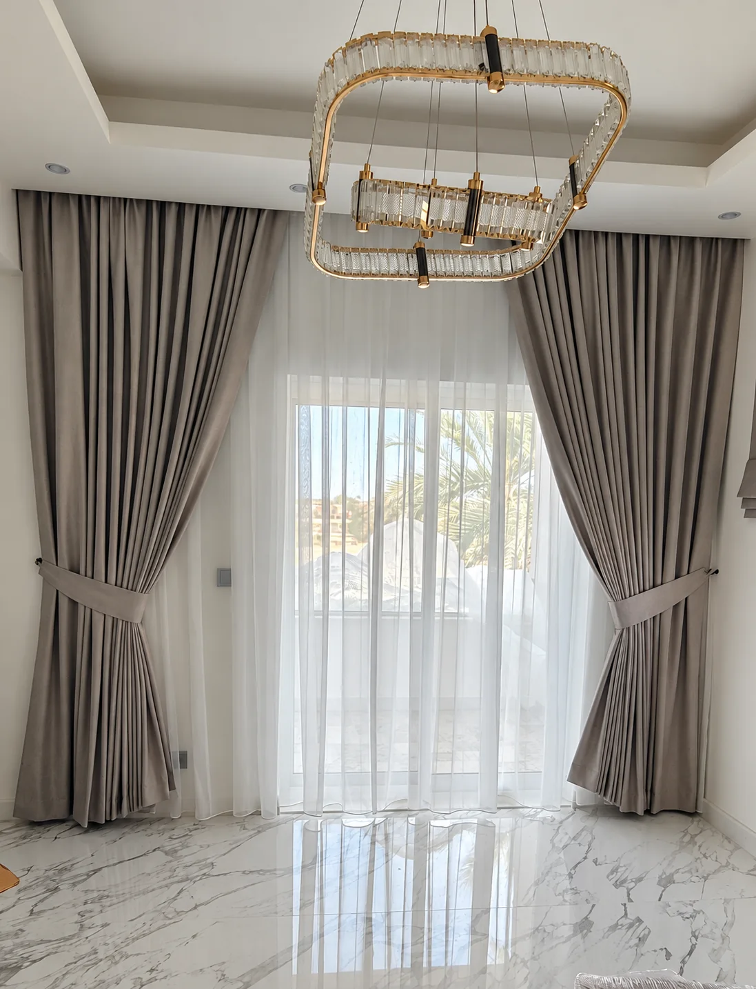 Grey drapes and a sheer under a crystal chandelier