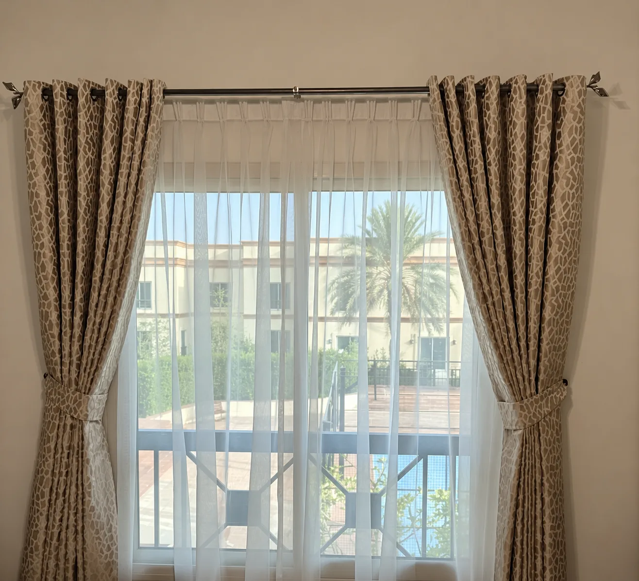 Patterned eyelet curtains on a chrome pole over a sheer, at a villa window